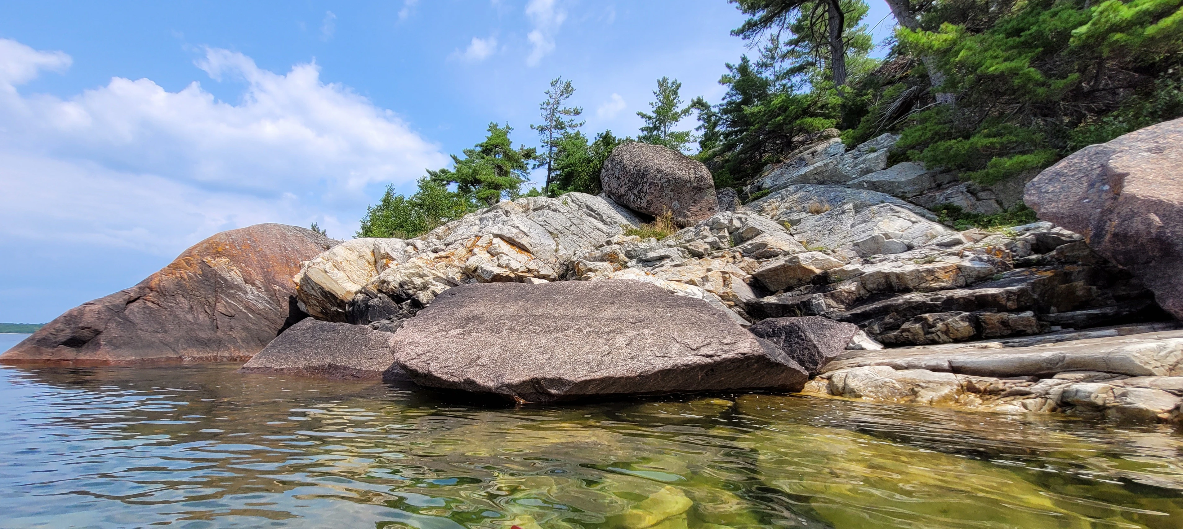 Western Shoreline of the Benjamind islands with red granite rock, white quartzite,
                trees and clear water